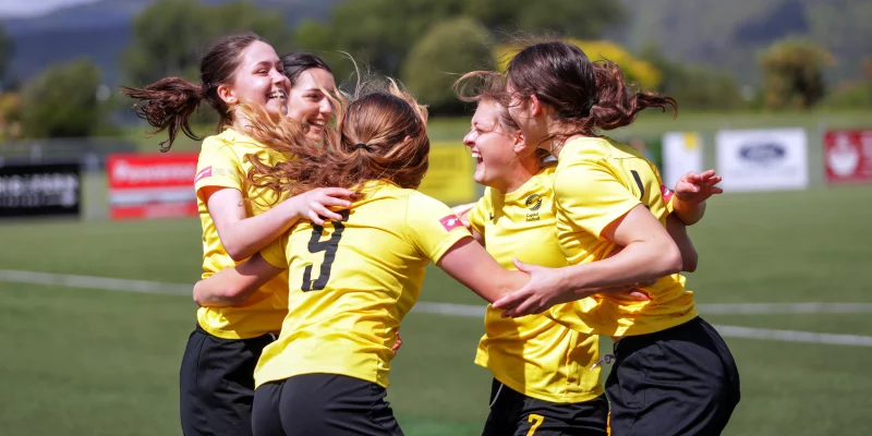 Girls arm-in-arm celebrating on a football pitch.