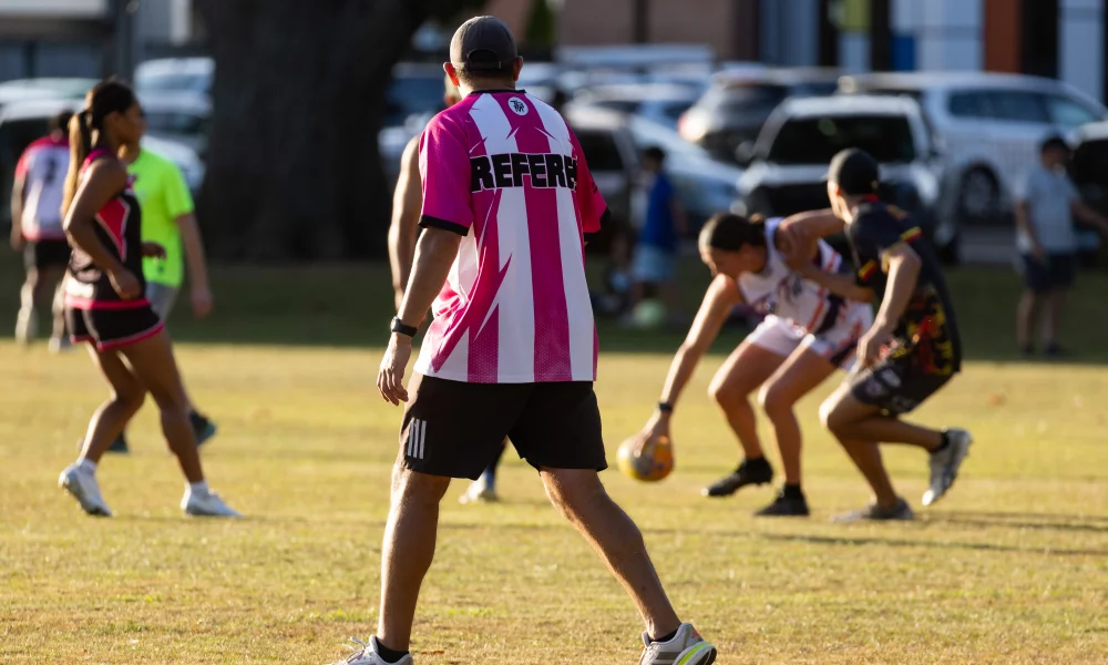 A rugby referee strides across the field reffing a women's community game.