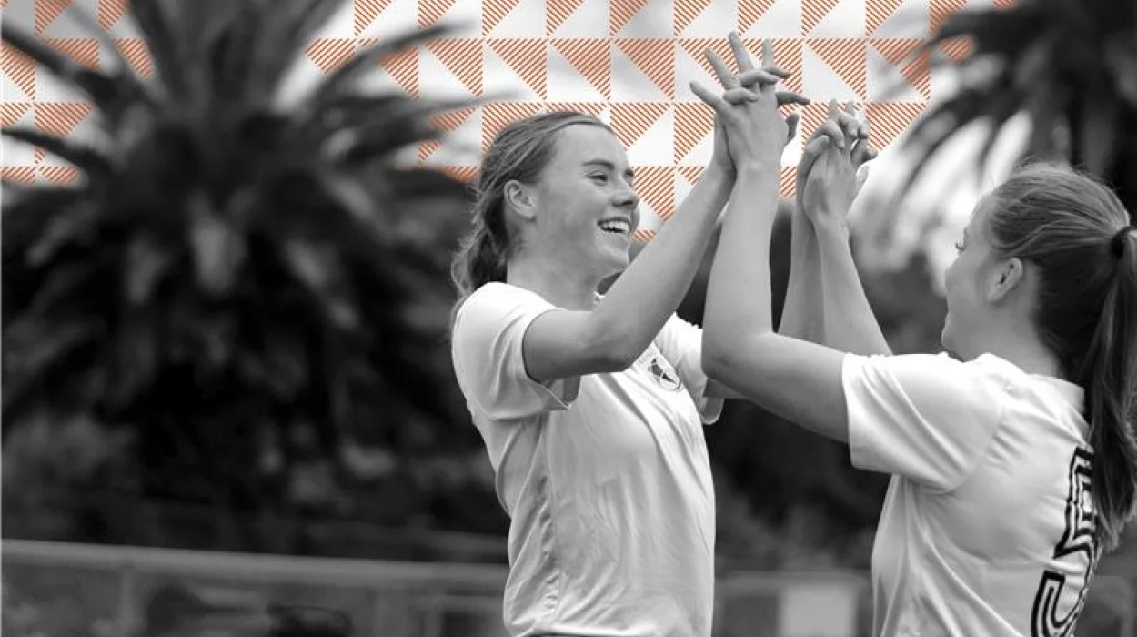Close-up of two girls in football kit doing a double high-five outdoors.