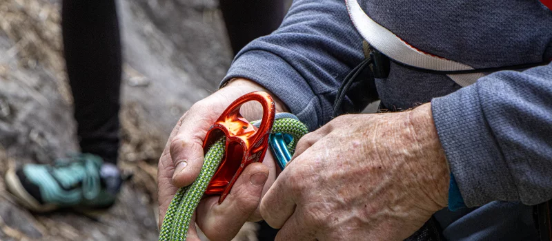 Close up of a man's hands clipping his climbing rope into his carabiner.