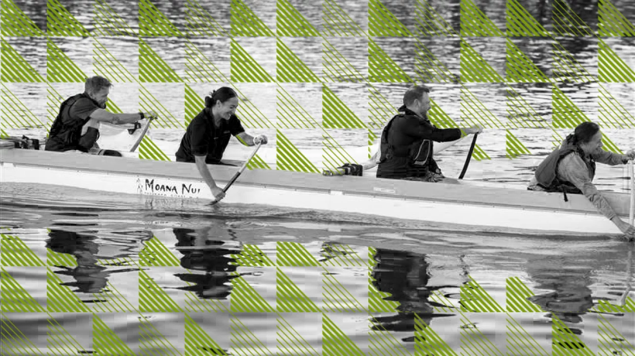 Four smiling people paddle a waka.